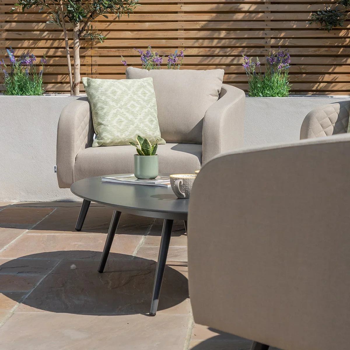 Beige outdoor armchair with green cushion beside round coffee table on patio