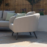 Beige outdoor armchair with black legs and green patterned cushions on patio