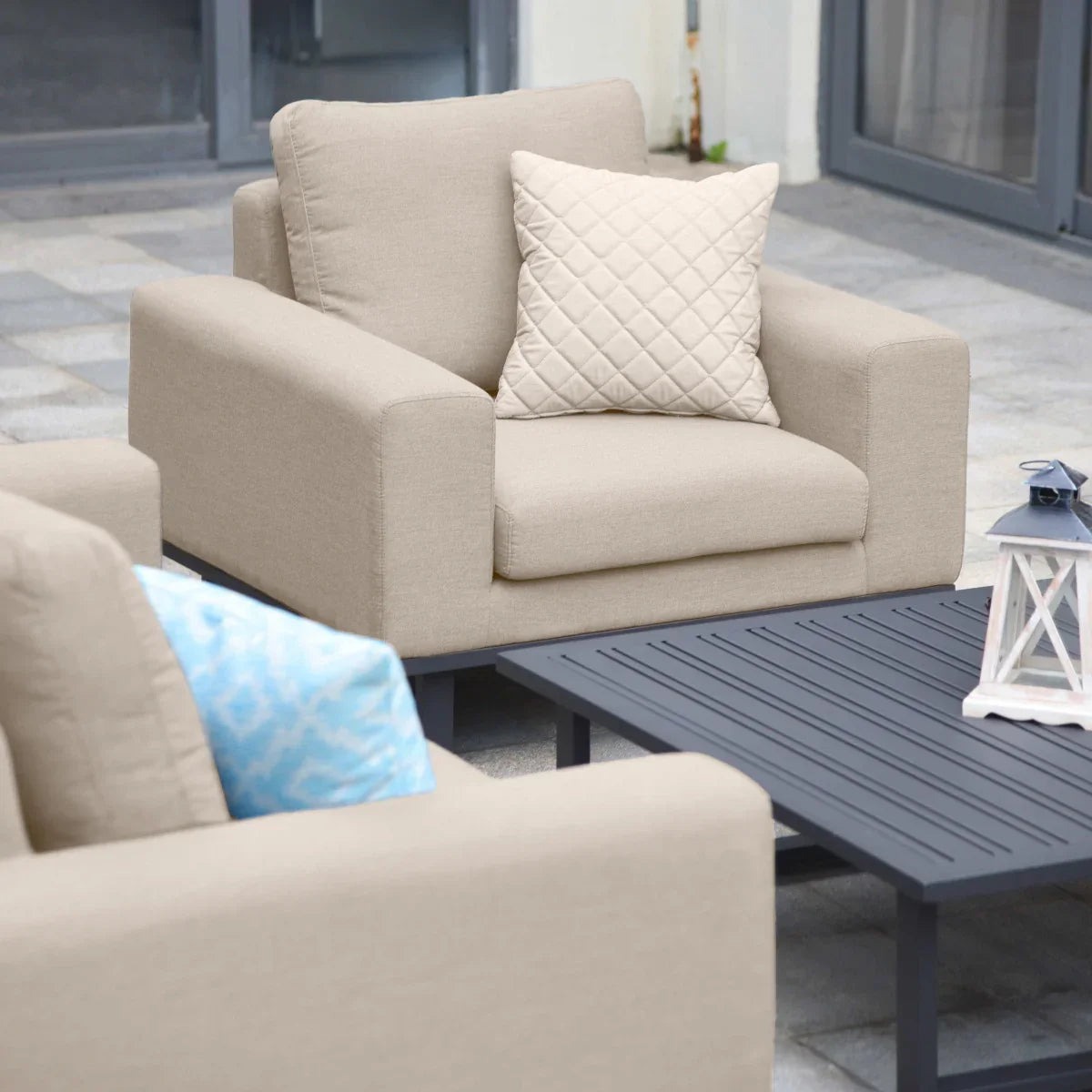 Beige outdoor armchair set with quilted cushion beside black slatted coffee table on patio