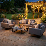 Grey outdoor sofa set with armchairs and coffee table on patio, evening garden setting
