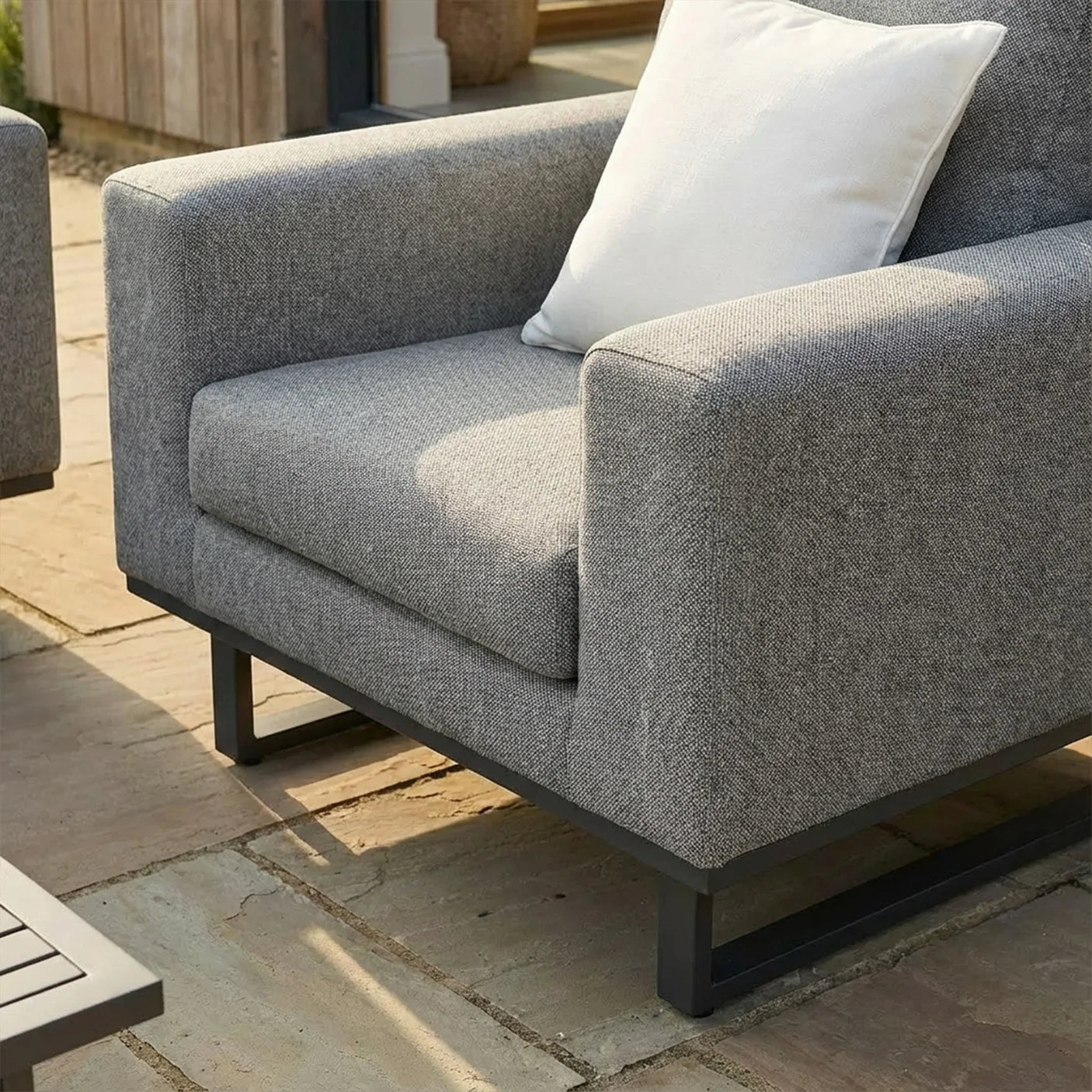 Grey outdoor armchair with metal base and white cushion on stone patio