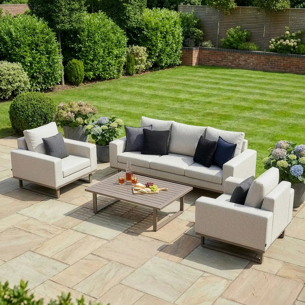 Light grey outdoor sofa set with matching armchairs and coffee table on patio, garden view