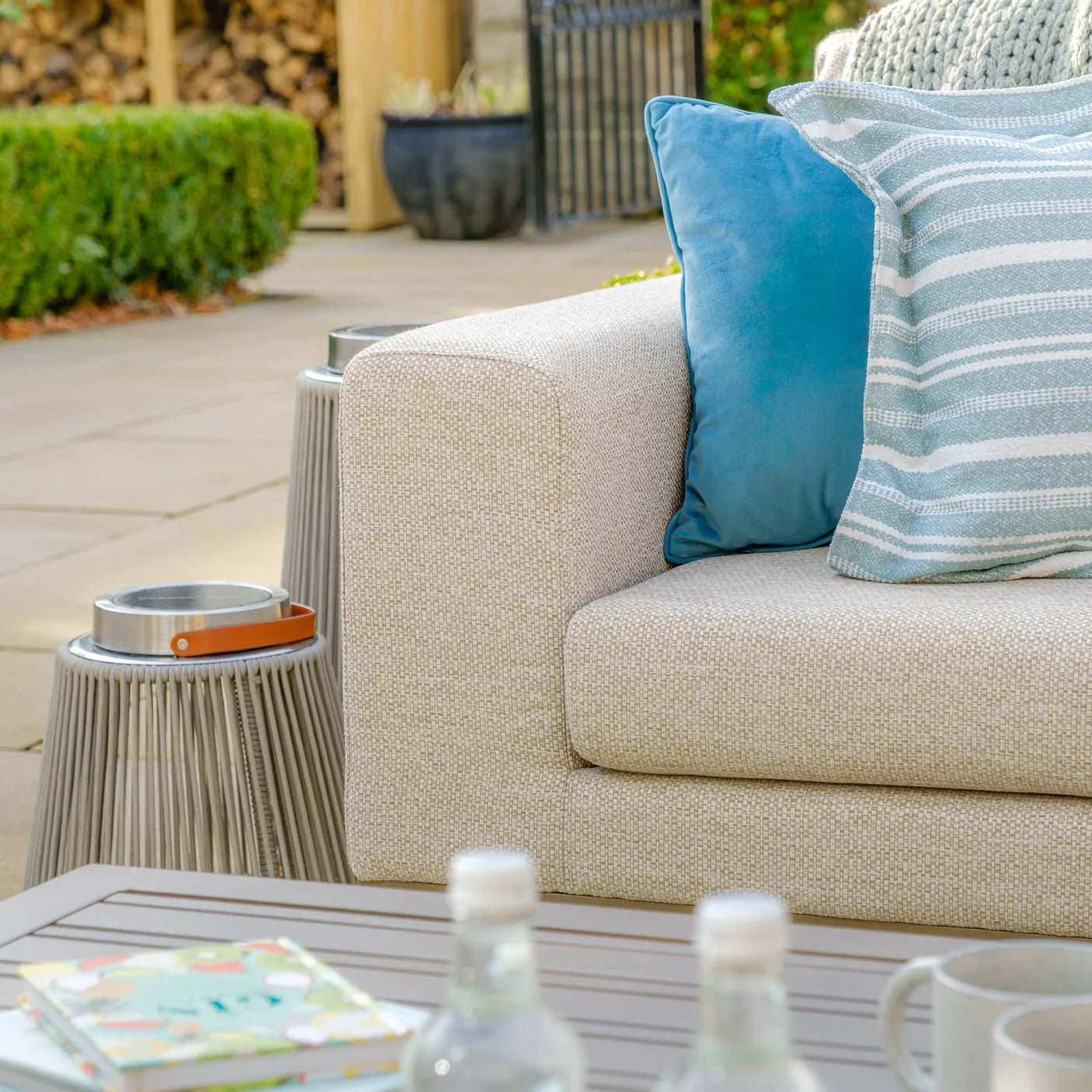 Beige outdoor sofa with blue and striped cushions on patio beside modern garden side table