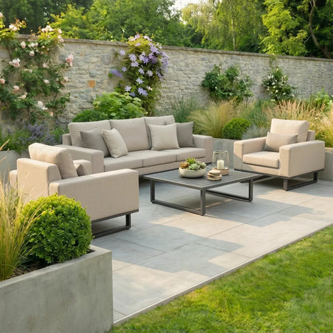 Beige outdoor sofa set with matching armchairs and coffee table on patio, garden backdrop