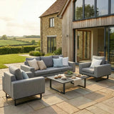 Grey outdoor sofa set with armchairs and table on a stone patio beside modern cottage