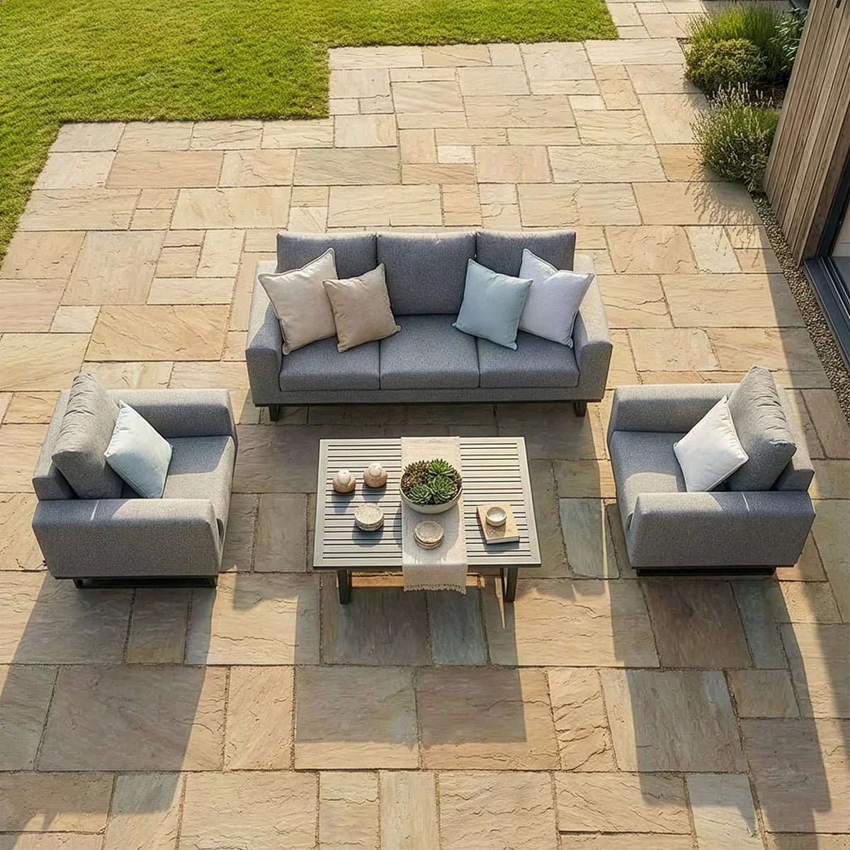 Grey outdoor sofa set with armchairs and coffee table on stone patio, neutral cushions included