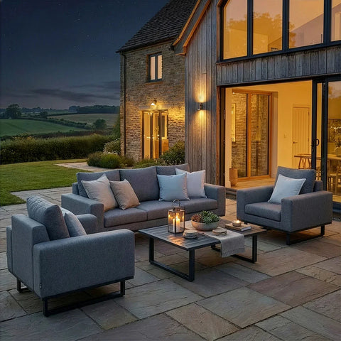 Grey outdoor sofa set with armchairs and cushions on stone patio, modern house in background