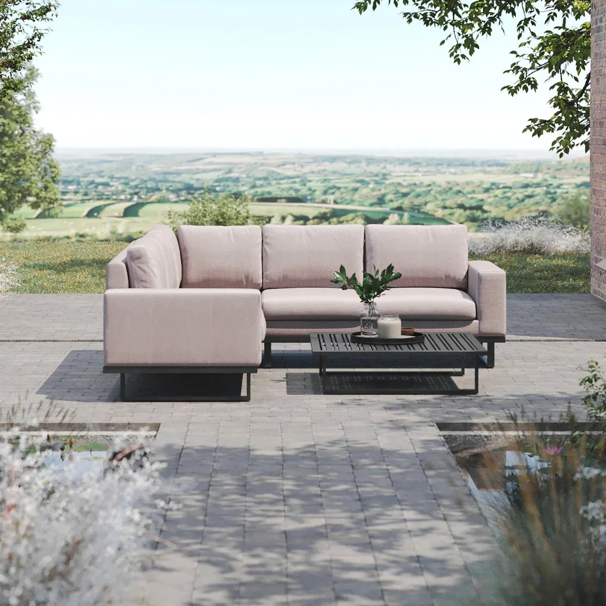 Light beige outdoor corner sofa with black coffee table on paved patio overlooking countryside