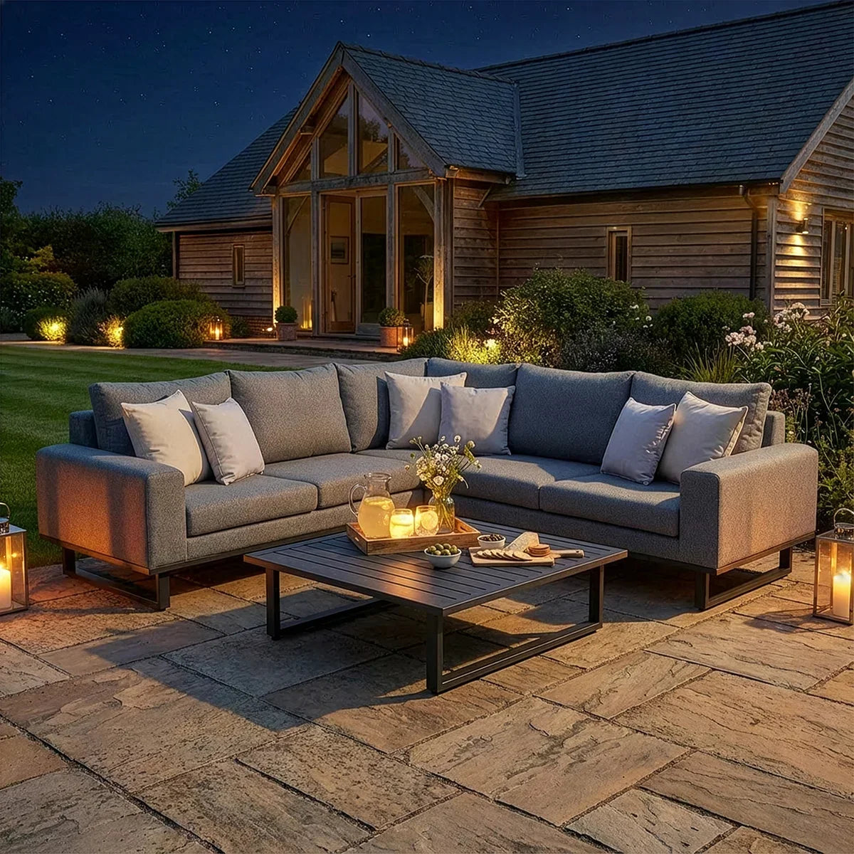 Grey outdoor corner sofa set with cushions and coffee table on stone patio at dusk