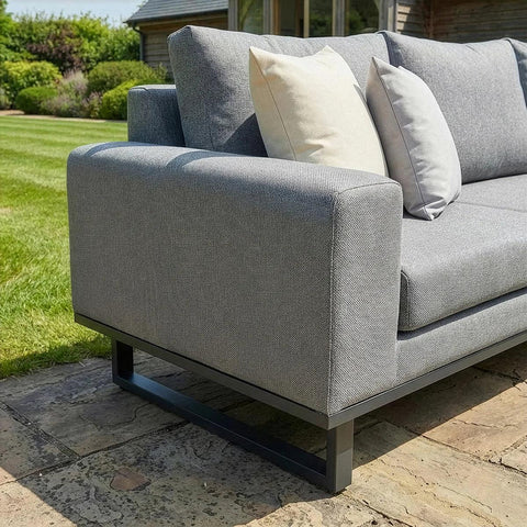 Grey outdoor sofa with metal frame and cushions on stone patio, garden background