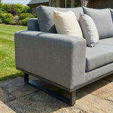Grey outdoor sofa with metal frame and cushions on stone patio, garden background