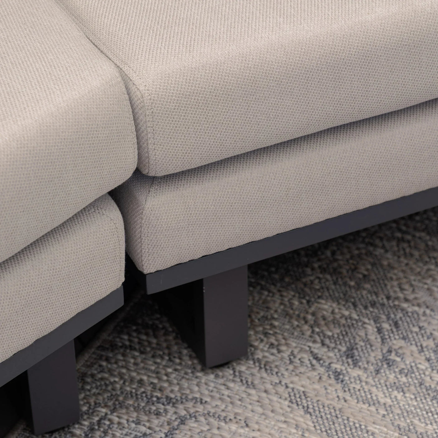 Closeup of grey fabric sofa corner with black legs on textured rug
