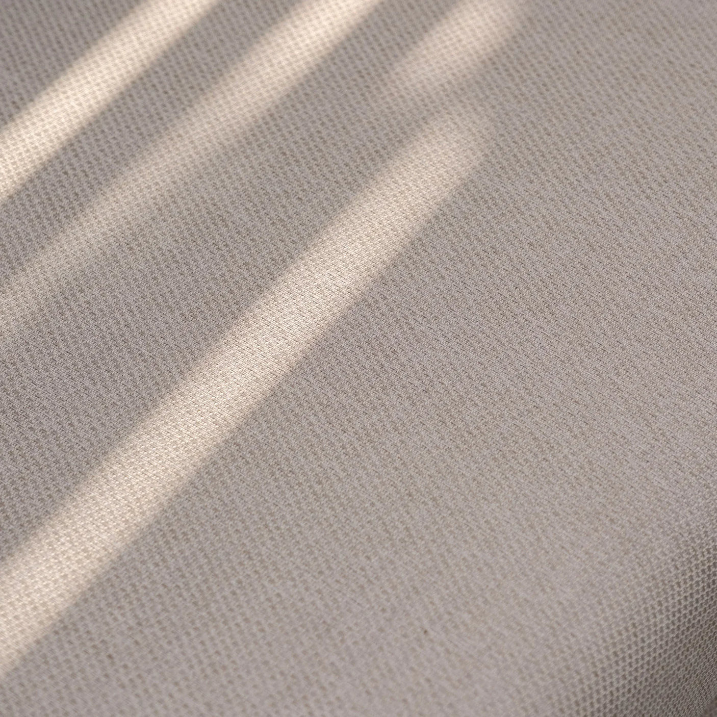 Beige fabric upholstery with subtle textured weave and natural sunlight shadows