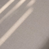 Beige fabric upholstery with subtle textured weave and natural sunlight shadows