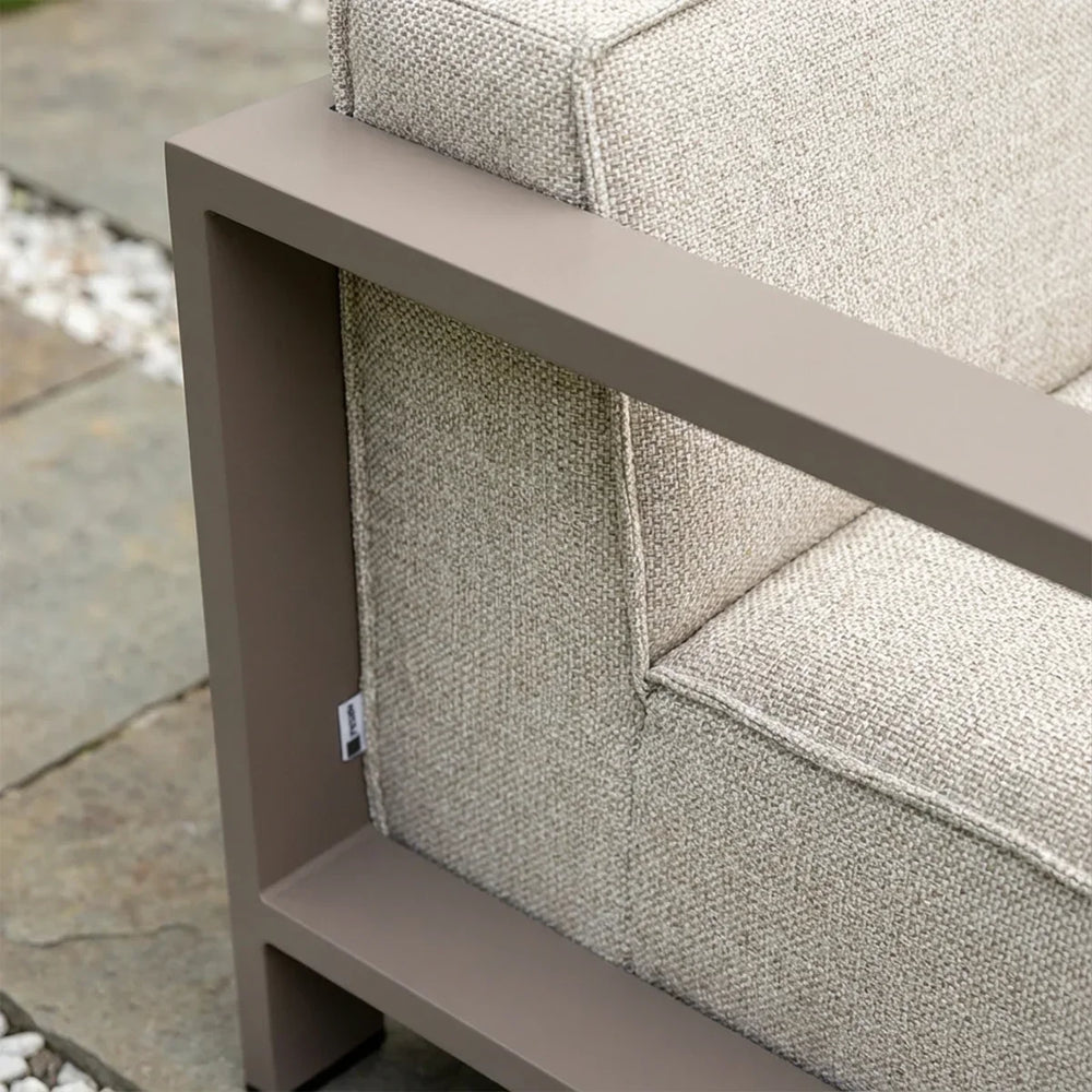 Closeup of textured beige outdoor sofa cushion with taupe metal armrest on stone patio