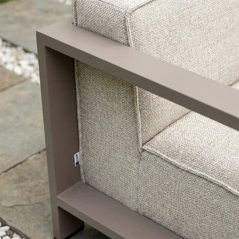 Closeup of textured beige outdoor sofa cushion with taupe metal armrest on stone patio