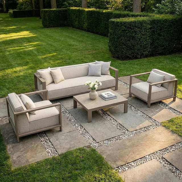 Beige outdoor sofa set with armchairs and coffee table on stone patio in garden setting