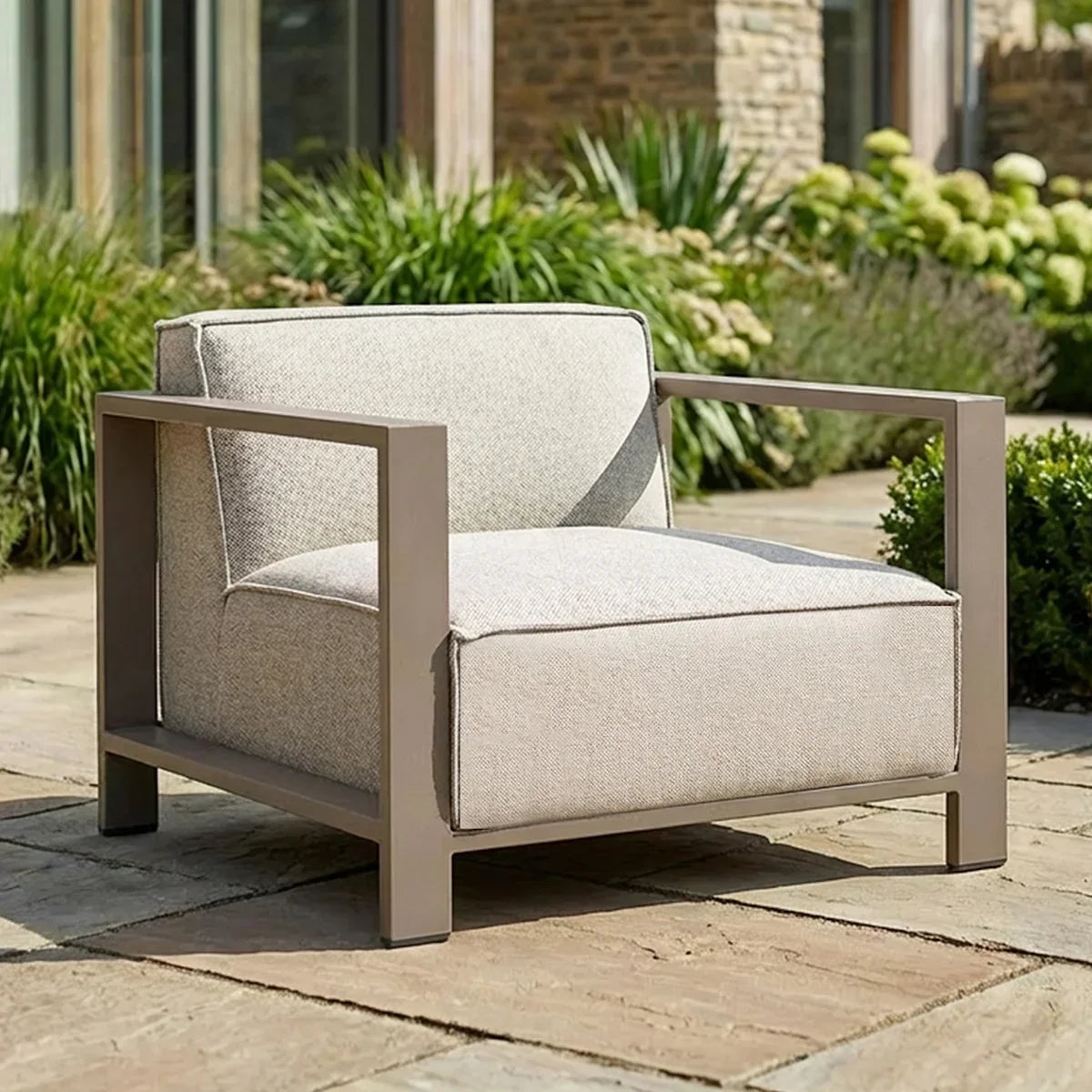 Beige outdoor armchair with metal frame and cushions on stone patio