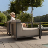 Modern outdoor armchair with grey cushions on a garden patio, woman seated in sunlight