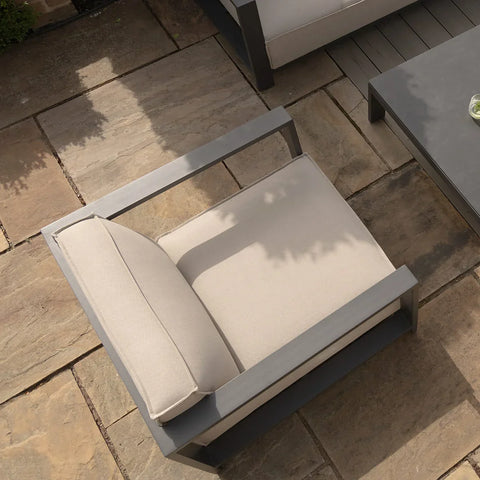 Beige outdoor armchair with metal frame on stone patio next to modern coffee table