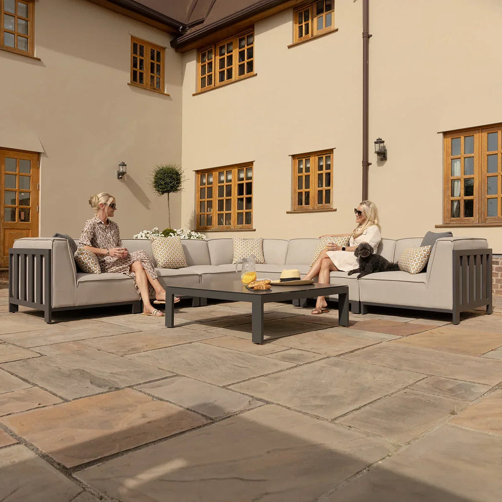 Grey outdoor corner sofa set with scatter cushions and coffee table on stone patio