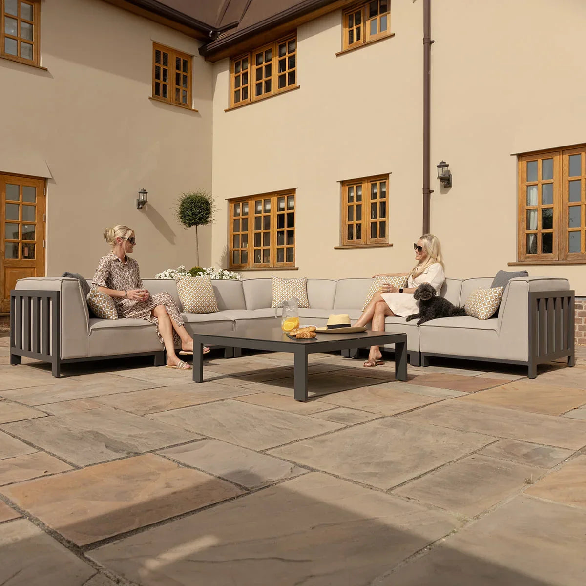 Grey outdoor corner sofa set with scatter cushions and coffee table on stone patio