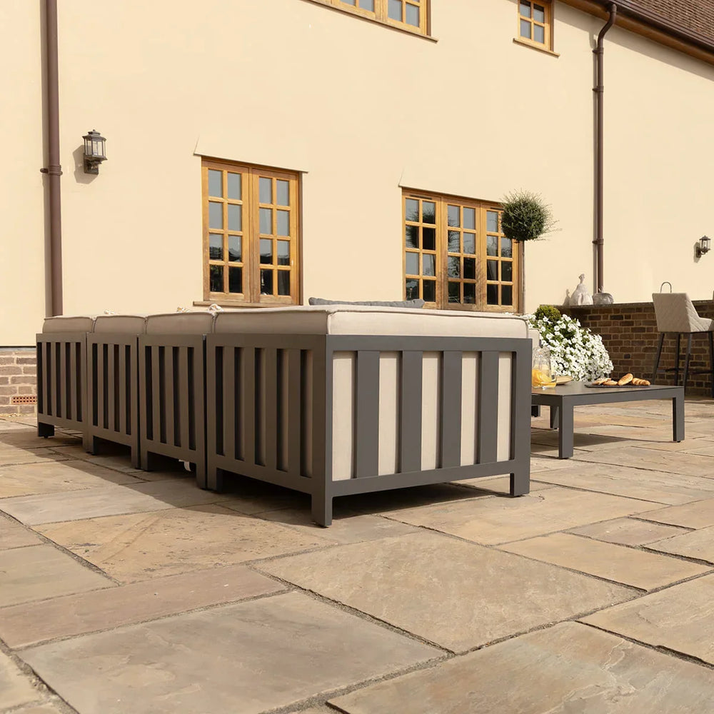 Grey outdoor sofa set with cushions on paved patio beside coffee table and decorative plants