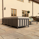 Grey outdoor sofa set with cushions on paved patio beside coffee table and decorative plants