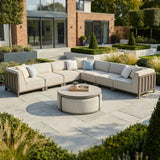 Beige outdoor corner sofa set with round coffee table on stone patio, modern garden setting
