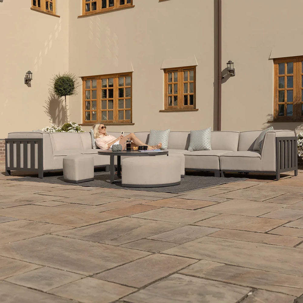 Grey outdoor corner sofa set with round coffee table and pouffes on stone patio