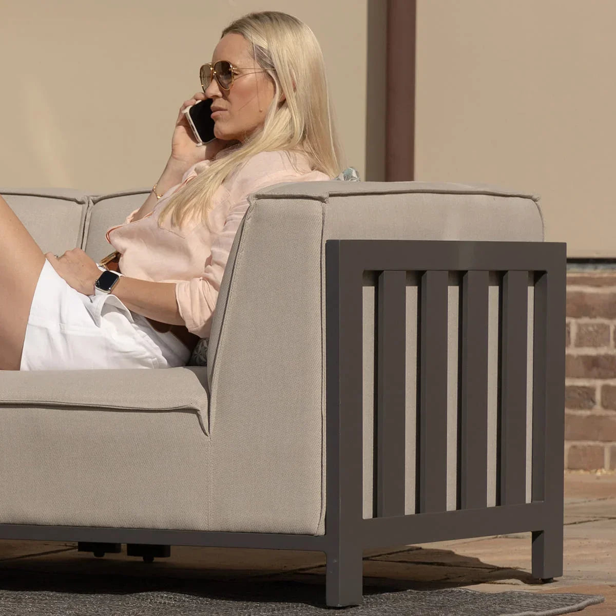 Beige outdoor sofa with grey metal frame, woman relaxing on patio furniture