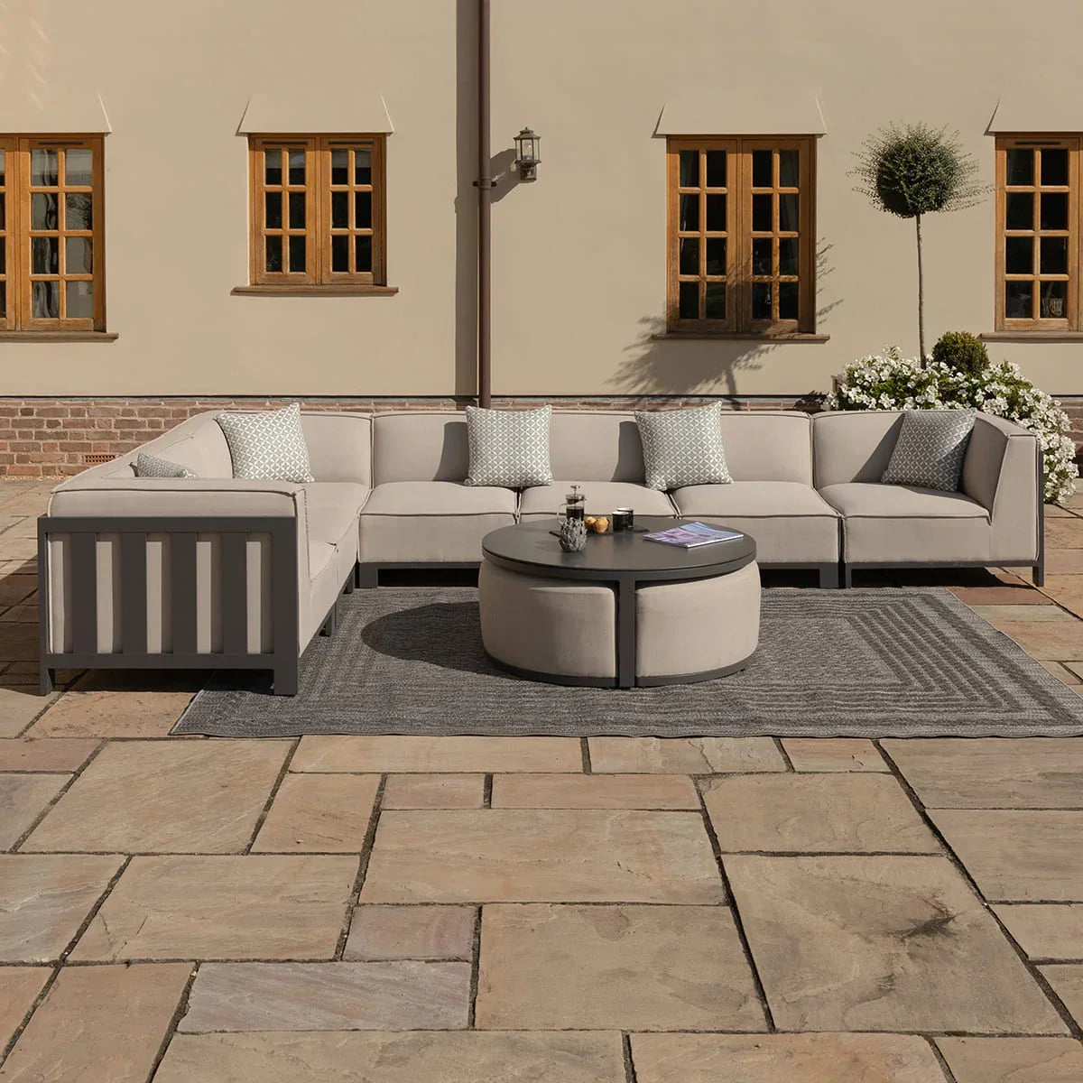 Beige outdoor corner sofa set with round coffee table and scatter cushions on a patio
