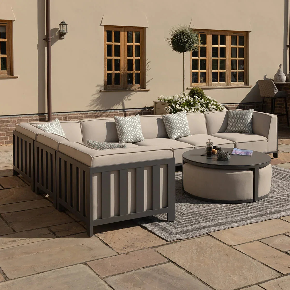 Outdoor corner sofa set with grey frame and beige cushions on patio, round coffee table in front