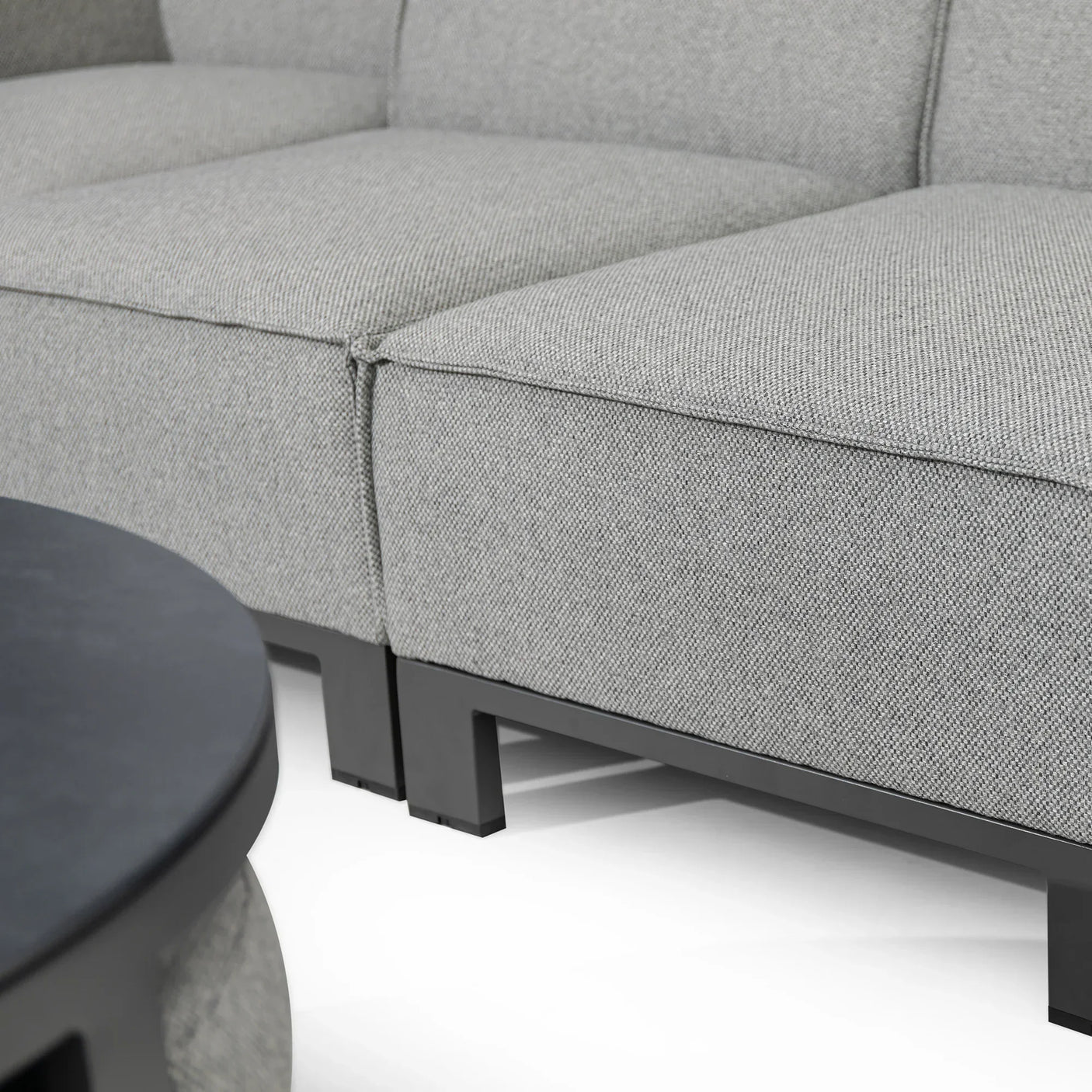 Closeup of modern grey fabric sofa with black metal legs and corner coffee table