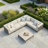 Beige outdoor corner sofa set with cushions and coffee table on stone patio, garden view