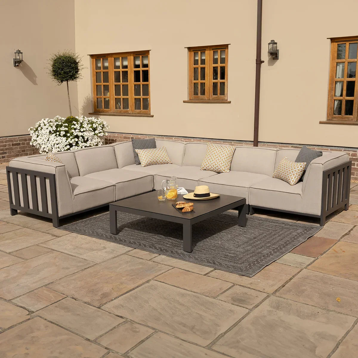 Grey outdoor corner sofa set with cushions and coffee table on stone patio