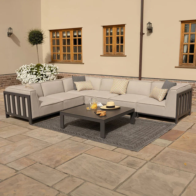 Grey outdoor corner sofa set with cushions and coffee table on stone patio
