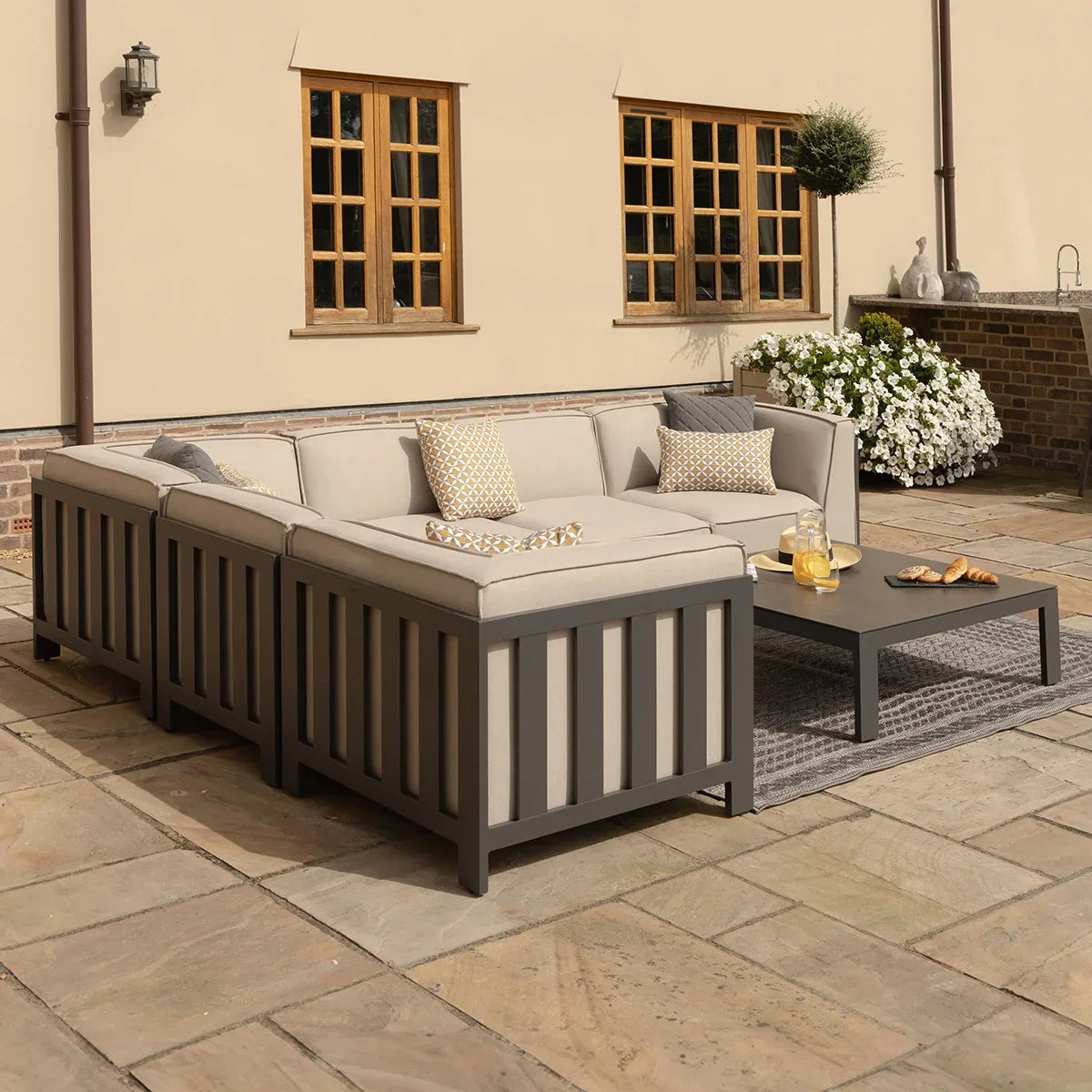 Grey outdoor corner sofa set with beige cushions and coffee table on stone patio