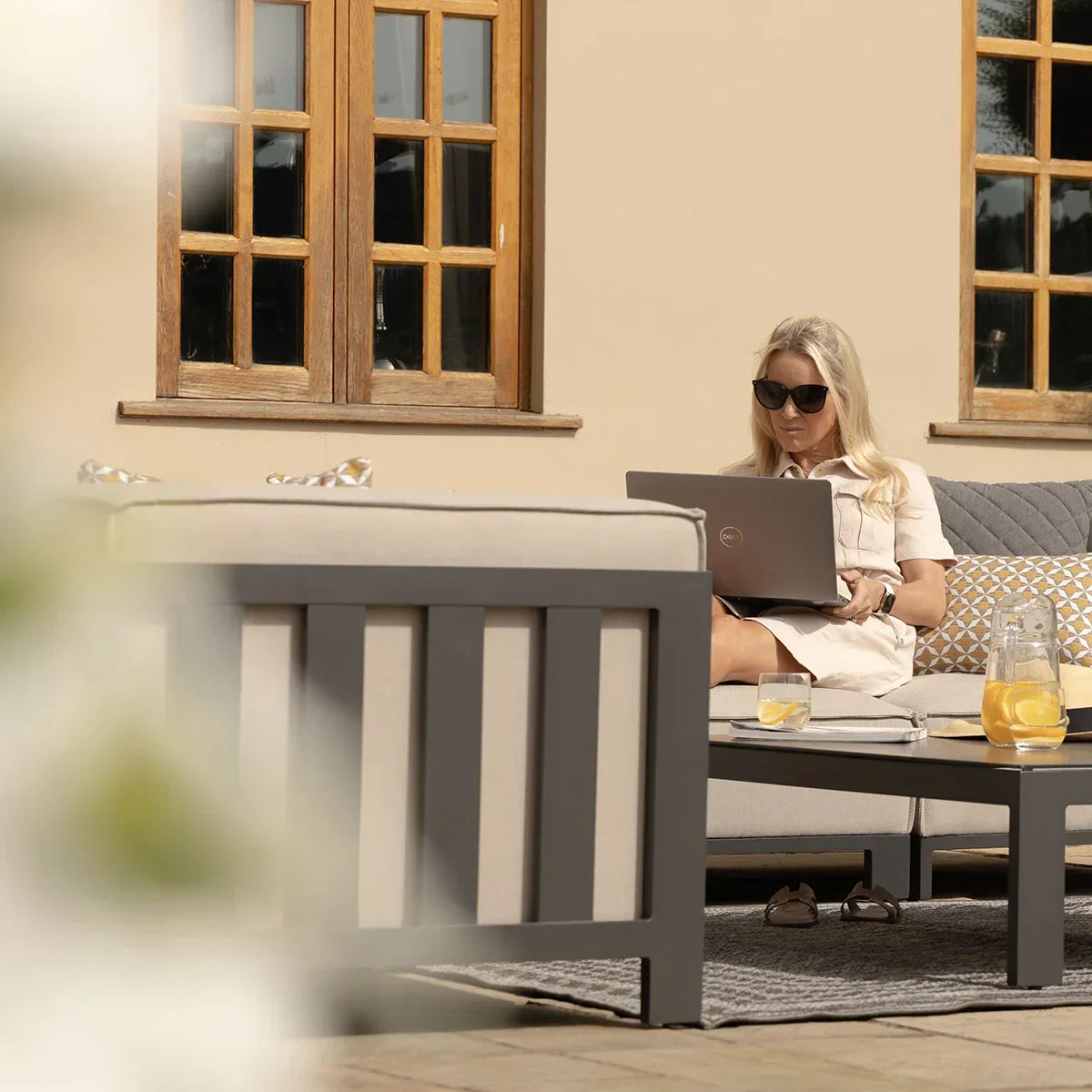 Outdoor grey garden sofa set with cushions and coffee table on patio, woman using laptop