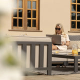 Outdoor grey garden sofa set with cushions and coffee table on patio, woman using laptop