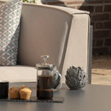 Outdoor fabric sofa with geometric cushion beside coffee press and muffins on table