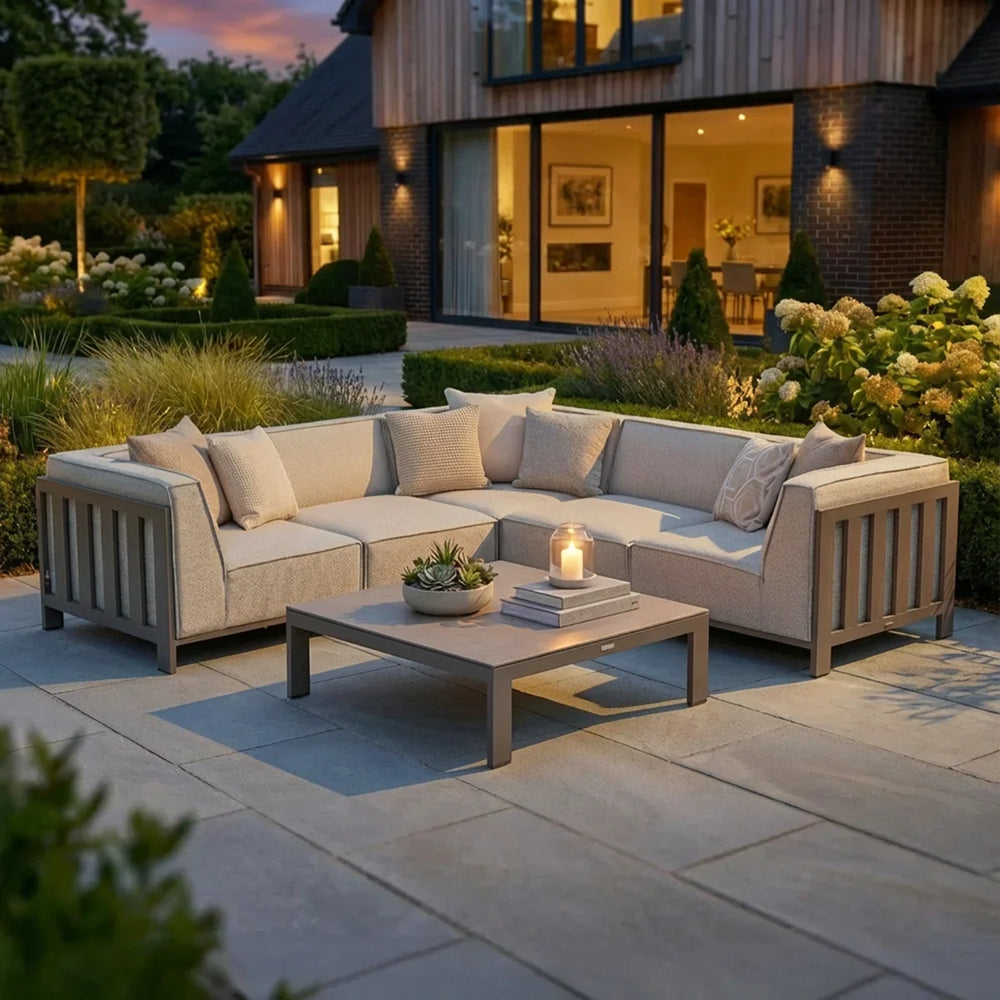 Beige outdoor corner sofa set with cushions and coffee table on stone patio at dusk
