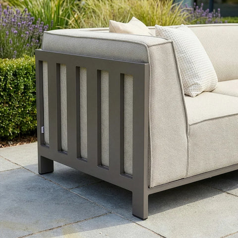 Outdoor sofa with taupe cushions and metal frame on patio beside garden shrubs and flowers