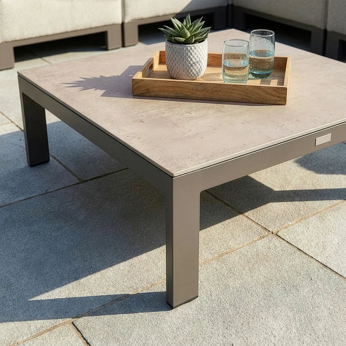 Modern outdoor coffee table with stone top, wooden tray, plant and glasses on patio