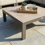 Modern outdoor coffee table with stone top, wooden tray, plant and glasses on patio