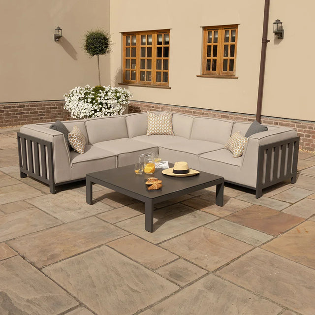 Outdoor corner sofa set with grey cushions and coffee table on a stone patio
