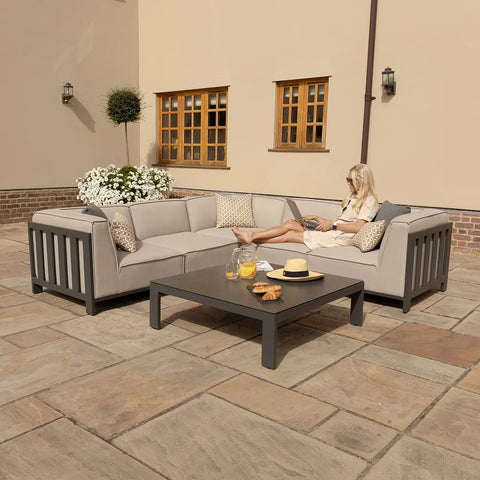 Grey outdoor corner sofa set with low coffee table on stone patio, cushions and snacks visible
