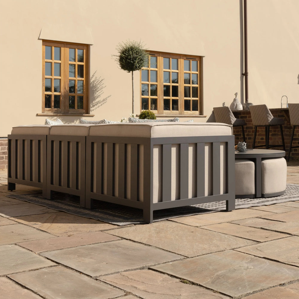 Grey outdoor sofa set with beige cushions on stone patio, matching ottoman and table