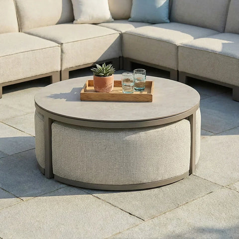 Round outdoor coffee table with beige fabric base, tray, plant and glasses on patio