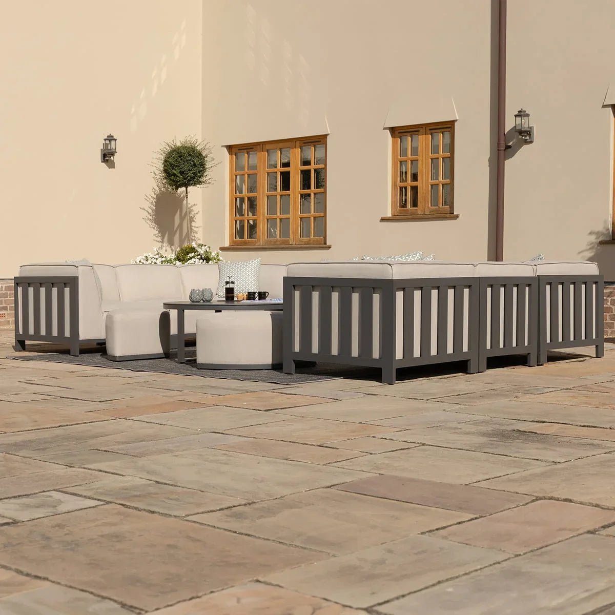 Grey aluminum outdoor sofa set with cream cushions and coffee table on stone patio